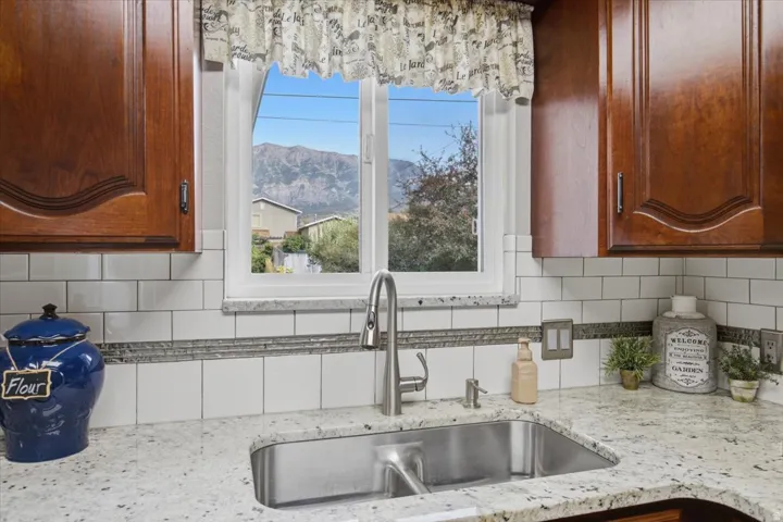 Granite countertops, subway tile backsplash, wood cabinetry, stainless steel sink, and a modern faucet