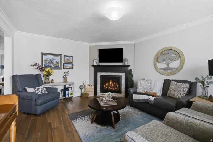 Living area featuring wood-finish flooring, a corner fireplace with a dark wood mantel and stone surround, and crown molding