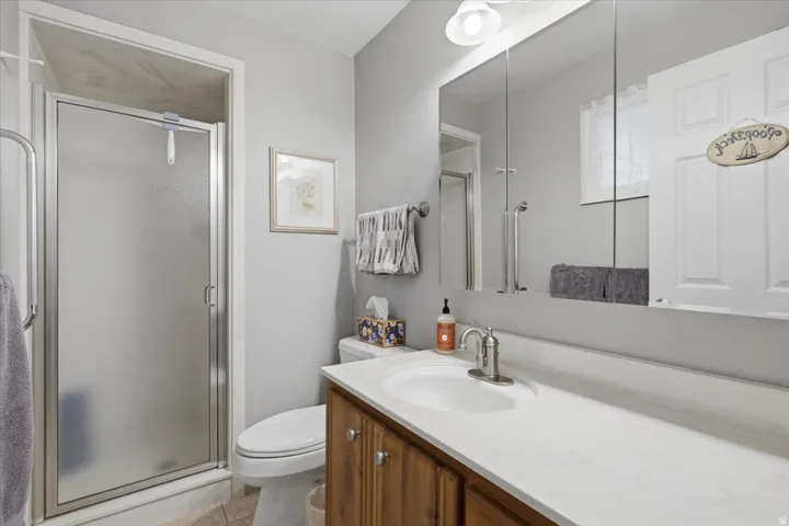 Frosted glass shower enclosure, wood-finish vanity with panel doors, white solid surface countertop, and mirrored medicine cabinet