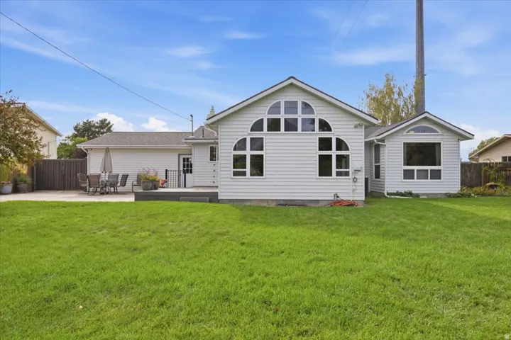 Expansive grassy yard with a concrete patio, wood deck, and white siding exterior