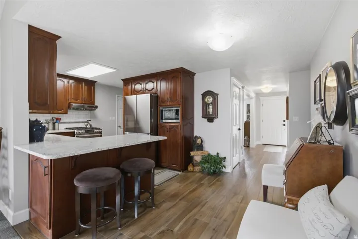 Kitchen featuring wood-finish cabinetry, stainless steel appliances, a white subway tile backsplash, and a breakfast bar with stone-finish countertops