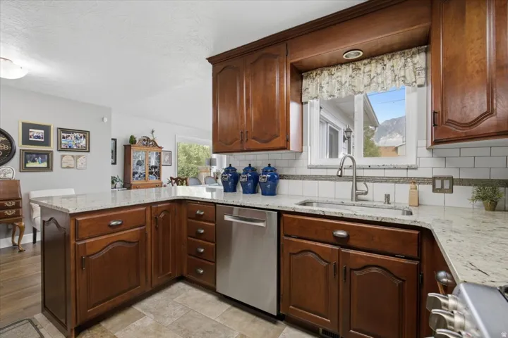 L-shaped kitchen featuring wood cabinetry, light-toned countertops, a stainless steel dishwasher, and a white subway tile backsplash