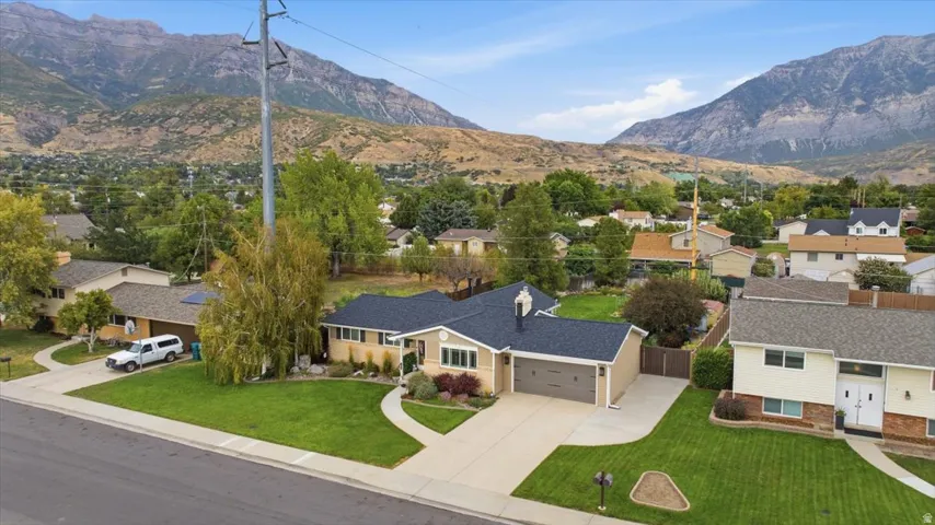 Mountain backdrop, manicured lawn, paved driveway, attached garage, and mature trees