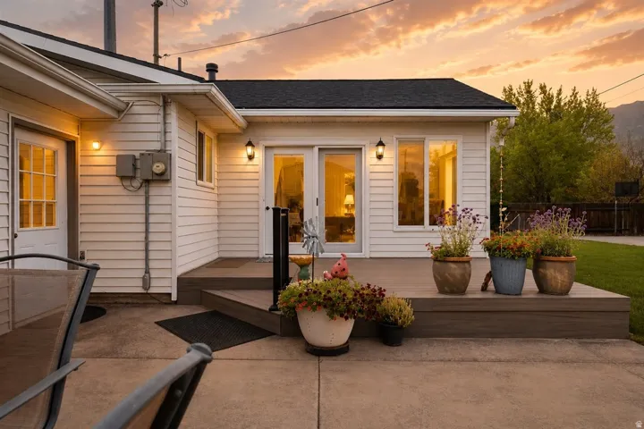 Exterior featuring white siding, a dark roof, a concrete patio, and a raised composite deck with black railing