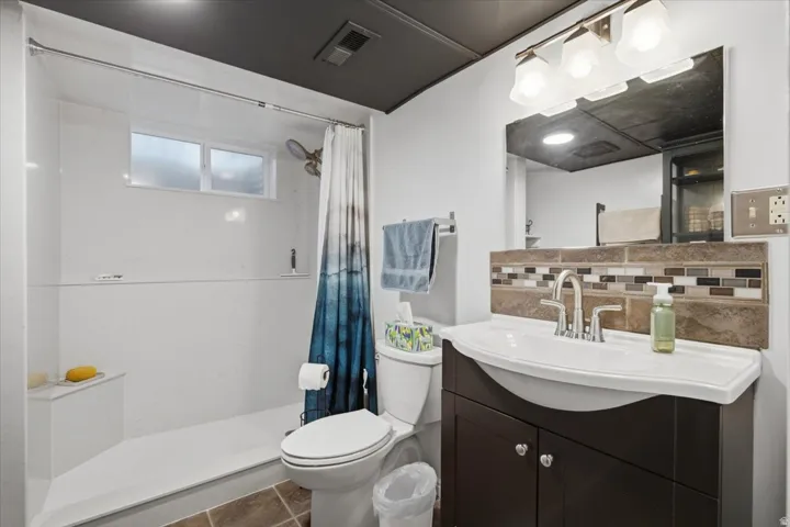 Built-in shower bench, vanity with integrated sink, mosaic tile backsplash, three-light vanity fixture, and brown floor tiling