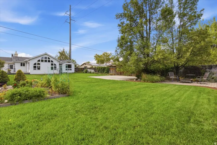 Expansive green lawn, mature trees, dedicated patio area, raised garden beds, and a white exterior structure with varied window designs