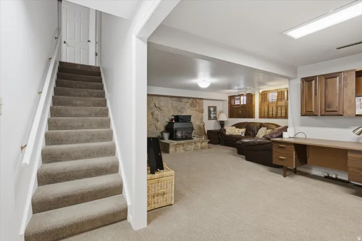 Carpeted stairs with white handrail, recessed wall alcove, wood-finish wall cabinetry, and stone-finish fireplace surround