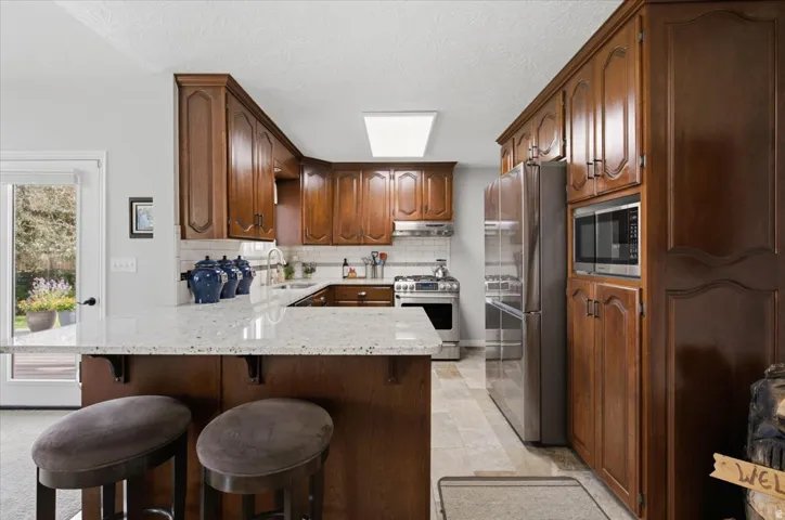 U-shaped kitchen featuring wood cabinetry, light-toned countertops, and stainless steel appliances
