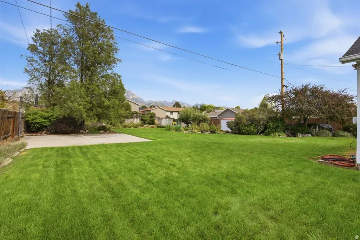 Expansive grassy area with mature trees, concrete pad, and mountain backdrop