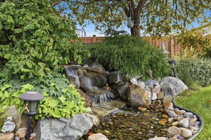 Water feature with cascading falls, river rock basin, surrounding boulders, mature landscaping, and integrated outdoor lighting