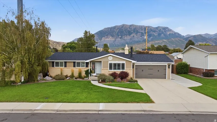 Single-story residence featuring a two-car garage, front walkway, and a landscaped yard with mature trees