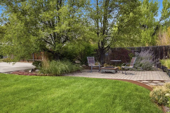 Expansive lawn with a stone paver patio, a built-in fire pit, mature trees, and a privacy fence