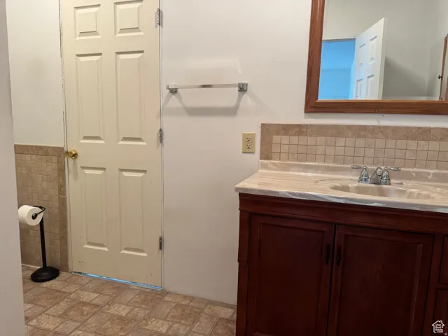 Wood-finish vanity with a light-toned countertop, tile backsplash, and ceramic tile flooring