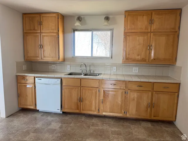Light wood-finish cabinetry, tile countertops, and a white dishwasher