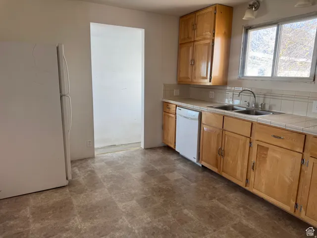 Kitchen featuring wood-finish cabinetry, a double basin stainless steel sink, a dishwasher, a refrigerator, and a tiled backsplash