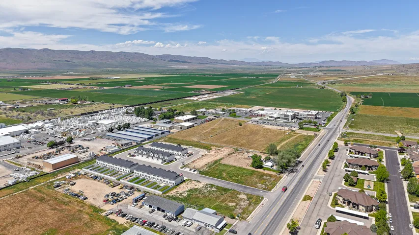 Expansive agricultural fields, distant mountain range, commercial properties, residential development, and thoroughfare