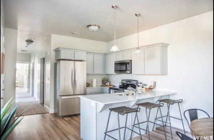 Kitchen featuring light-toned cabinetry, stainless steel appliances, a breakfast bar with pendant lighting, and wood-finish flooring