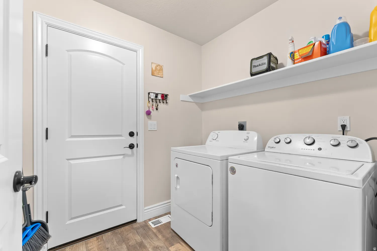 Laundry area featuring wood-finish flooring, built-in shelving, and a paneled door with matte black hardware