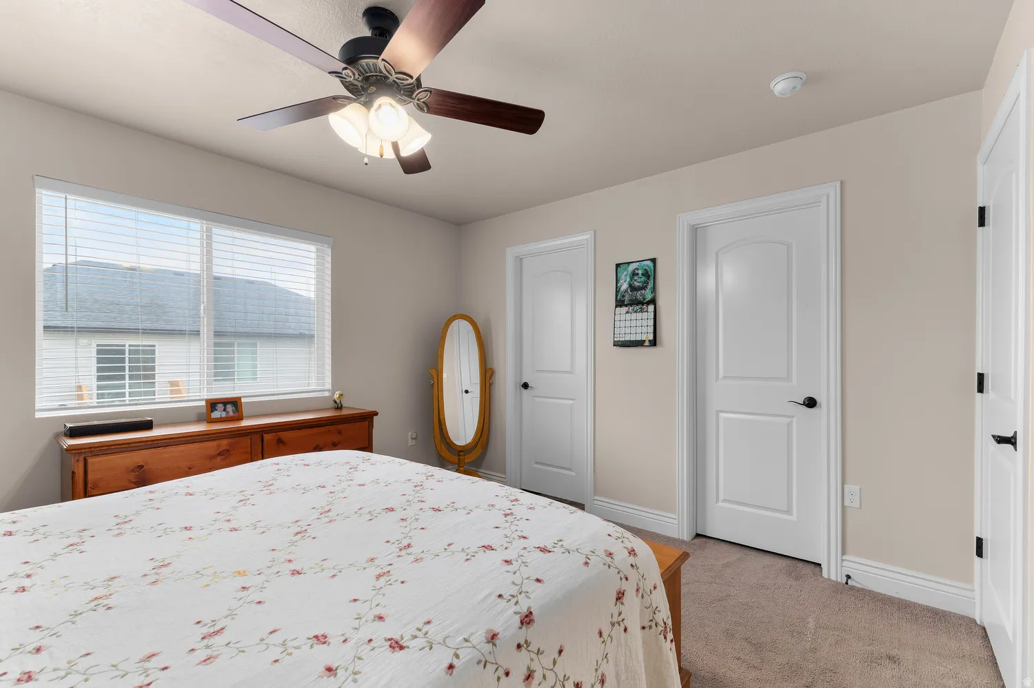 Spacious primary bedroom featuring neutral carpeting, a ceiling fan with integrated lighting, large double-hung windows with plantation shutters, and direct access to multiple closets and en-suite facilities
