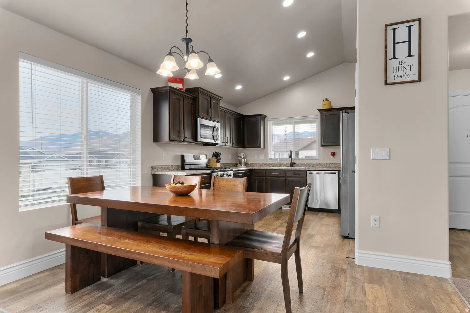 Vaulted ceiling with recessed lighting, wood-finish flooring, dark wood cabinetry, stainless steel appliances, and a double window