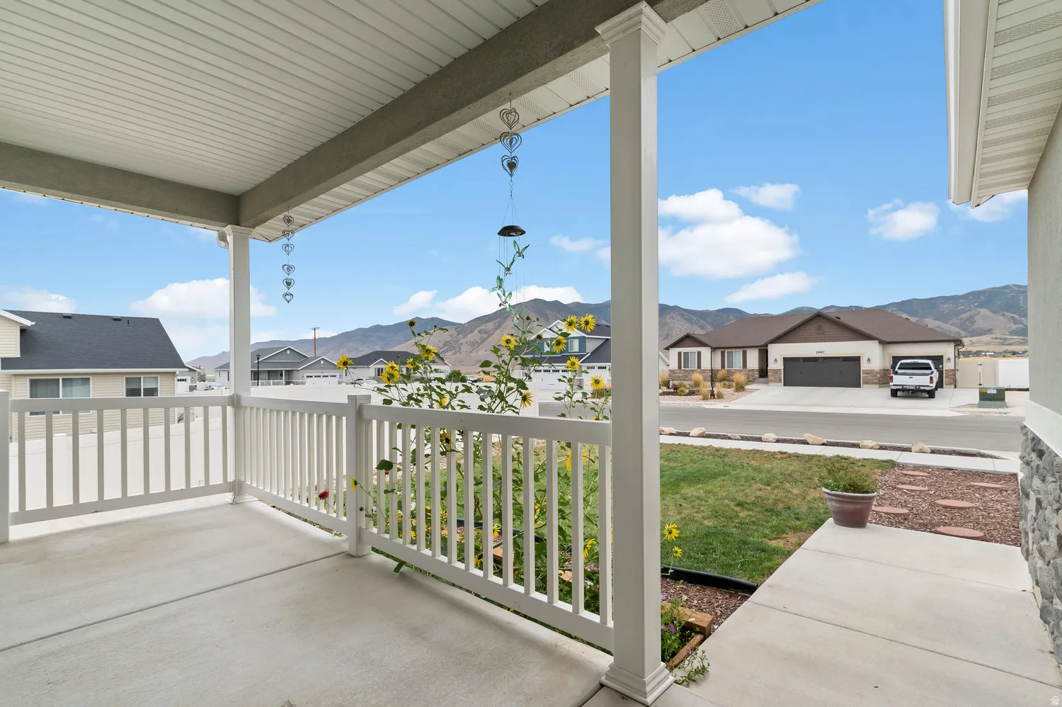 Covered front porch with white railing, concrete flooring, and stone facade accents