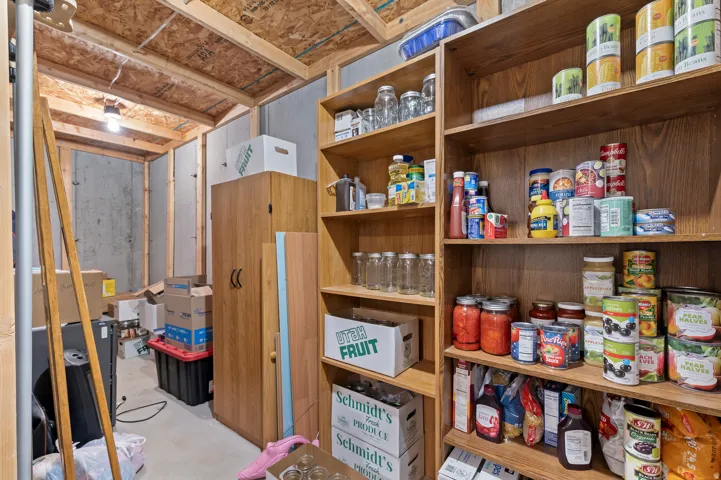 Unfinished basement space featuring exposed wooden ceiling joists, concrete walls, and extensive built-in shelving