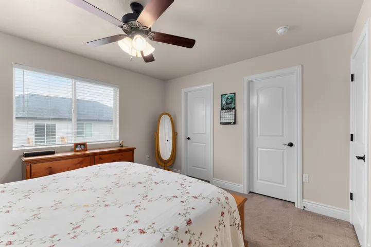 Spacious primary bedroom featuring neutral carpeting, a ceiling fan with integrated lighting, large double-hung windows with plantation shutters, and direct access to multiple closets and en-suite facilities