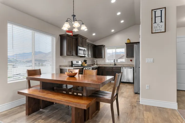 Vaulted ceiling with recessed lighting, wood-finish flooring, dark wood cabinetry, stainless steel appliances, and a double window