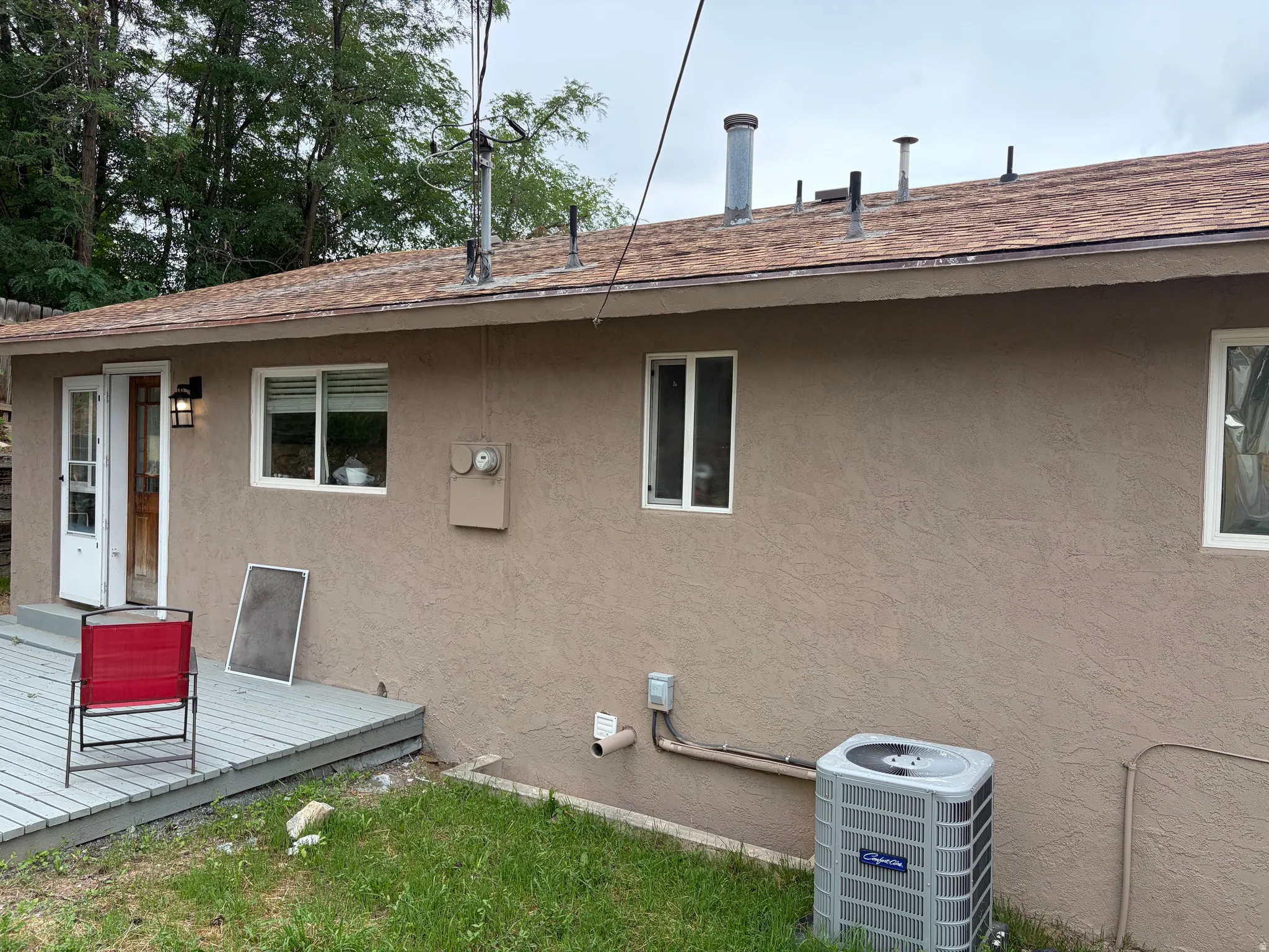 Stucco exterior with multiple windows, a wood-finish deck, and a central air conditioning unit