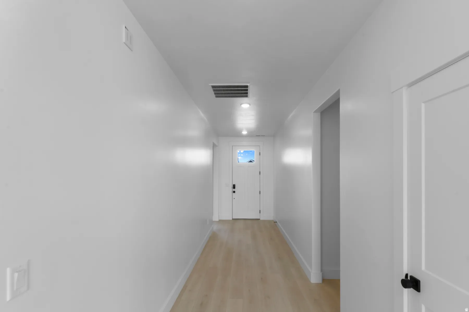 Hallway with wood-finish flooring, recessed lighting, and a white paneled door