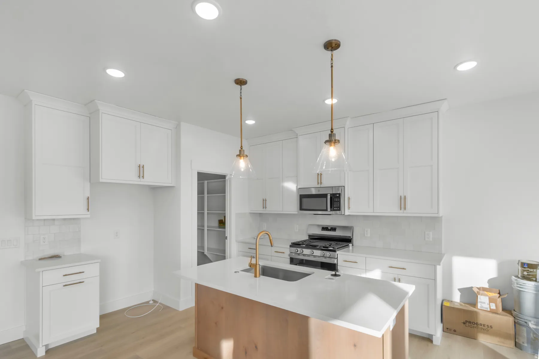 Kitchen featuring white shaker-style cabinetry, a built-in microwave, stainless steel range, a pantry, and a center island with a sink