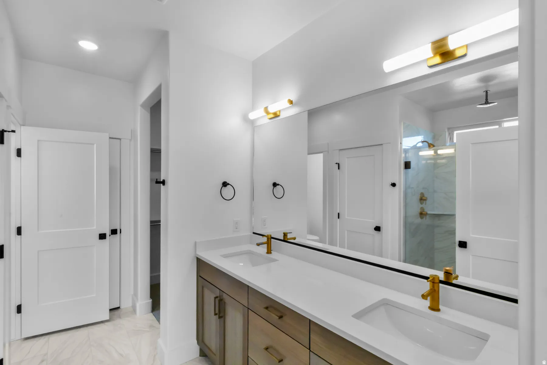Dual vanity with undermount sinks and brass-finish fixtures, large mirror, and glass-enclosed shower with tile surround