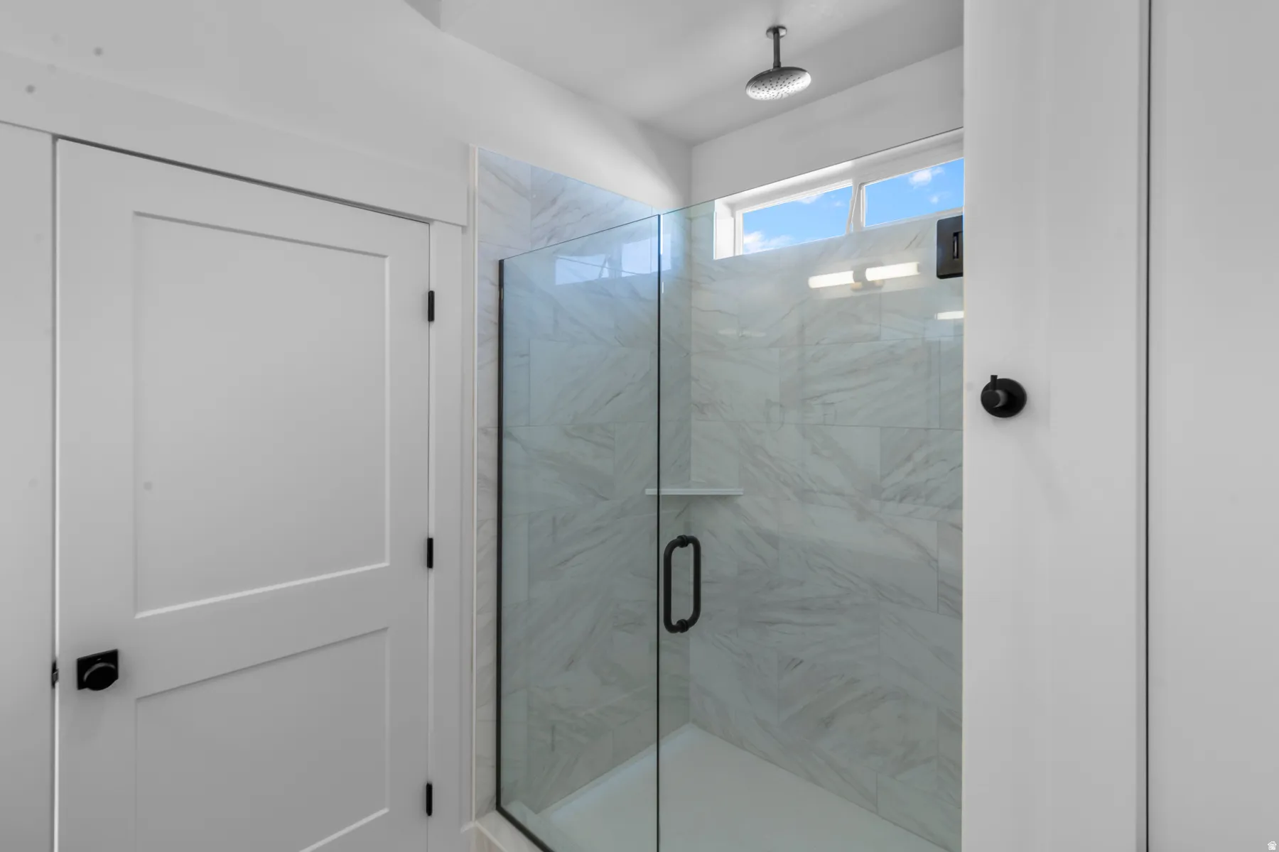 Glass-enclosed shower with white tiled walls, a built-in shelf, and a rain showerhead