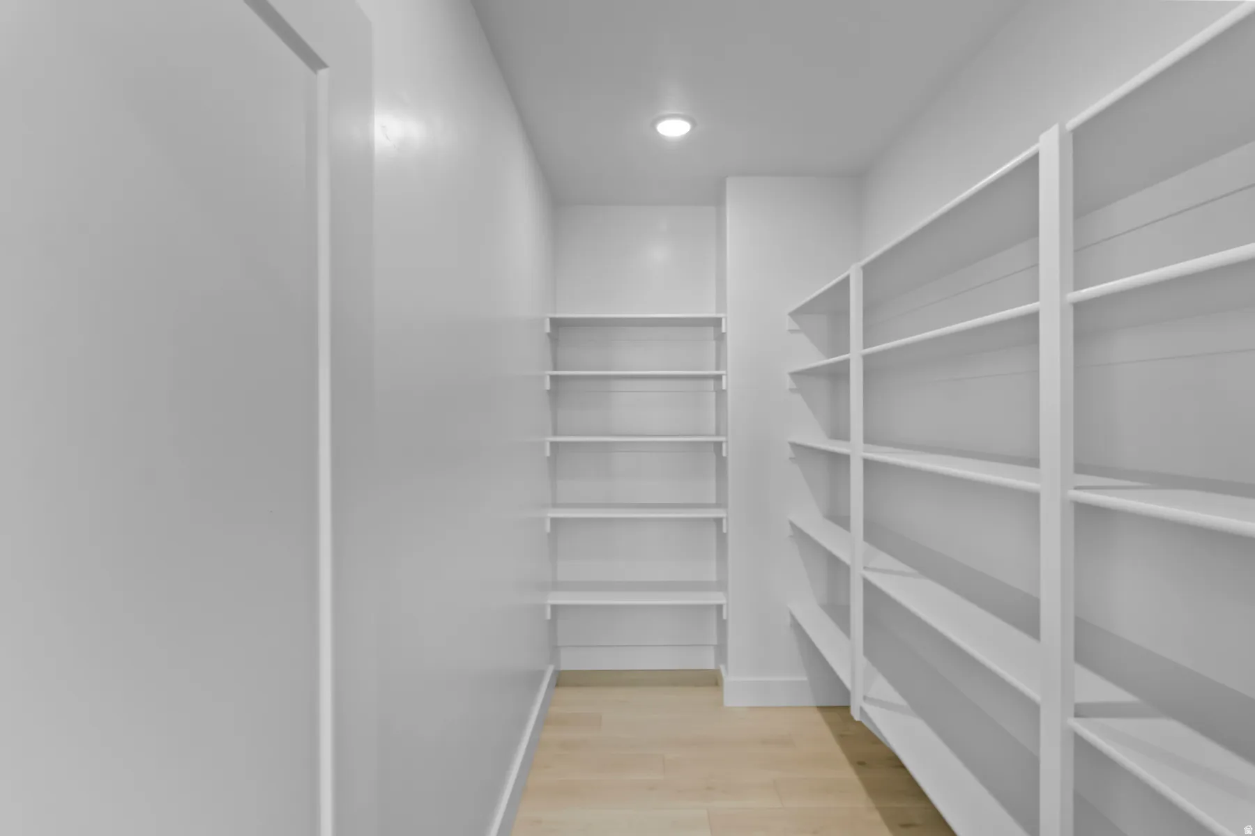Dedicated pantry space featuring extensive built-in shelving, recessed ceiling lighting, and light wood-finish flooring