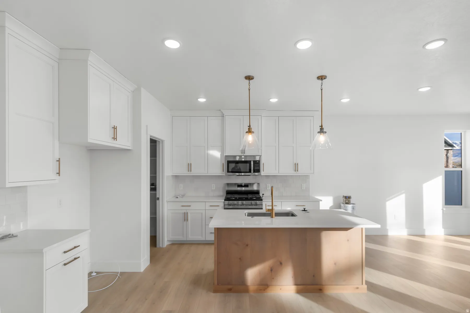 Kitchen featuring white shaker cabinetry, an island with wood-finish paneling and a light-toned countertop, stainless steel appliances, and pendant lighting