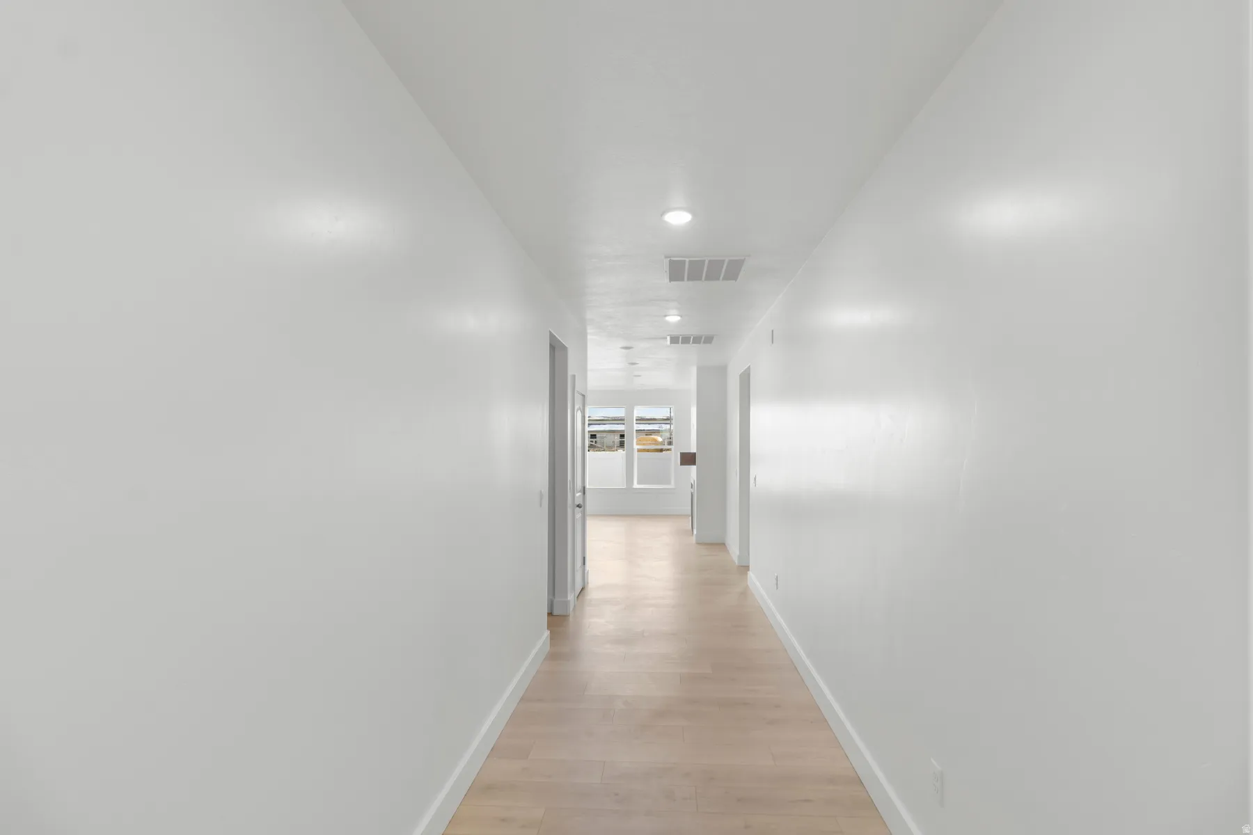 Recessed lighting, light wood-finish flooring, and white walls throughout