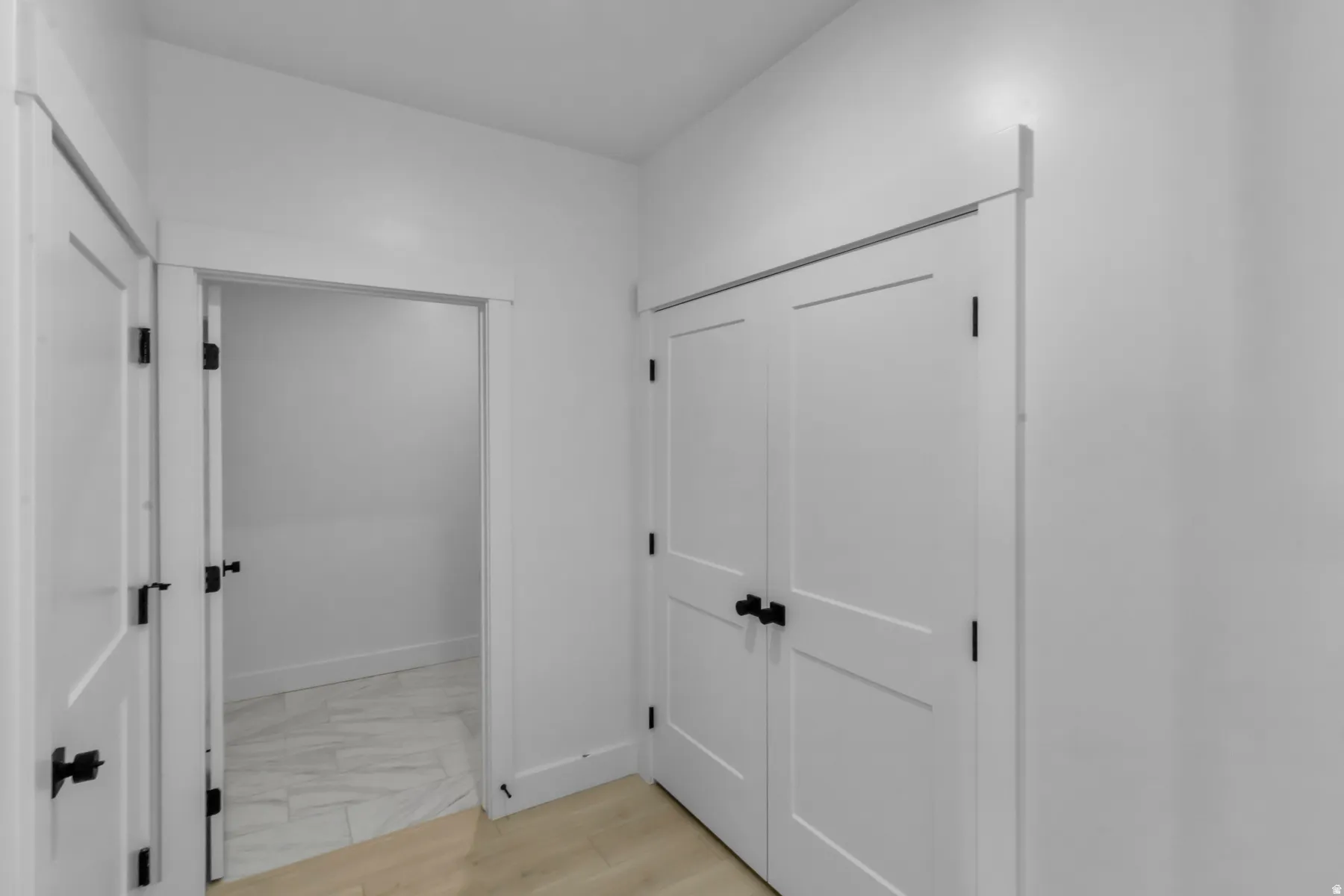 White interior doors with matte black hardware, light-toned wood-finish flooring, and white wall finishes
