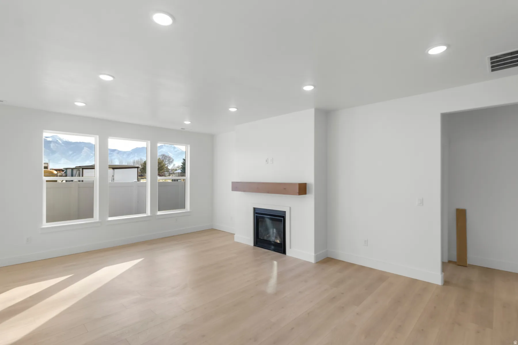 Spacious room featuring light wood-finish flooring, recessed lighting, and a modern fireplace with a wood mantel