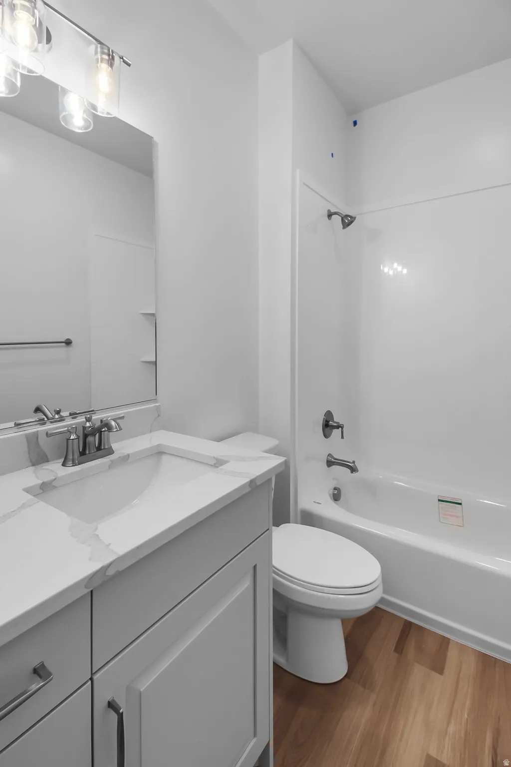 Vanity with an integrated rectangular sink, wood-finish flooring, and a full bathtub with shower