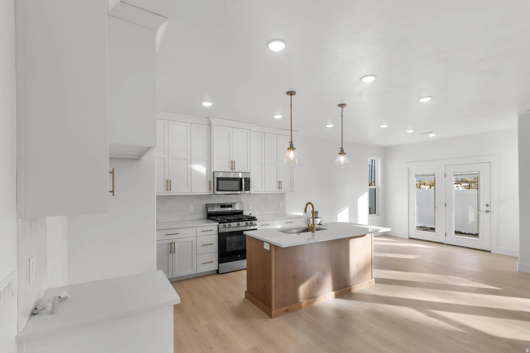 Gourmet kitchen featuring white shaker cabinetry, stainless steel appliances, a center island with pendant lighting, and light wood-finish flooring
