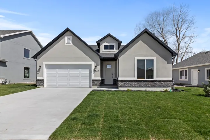 Modern stucco exterior with stone accents, an attached two-car garage, manicured lawn, and a concrete driveway