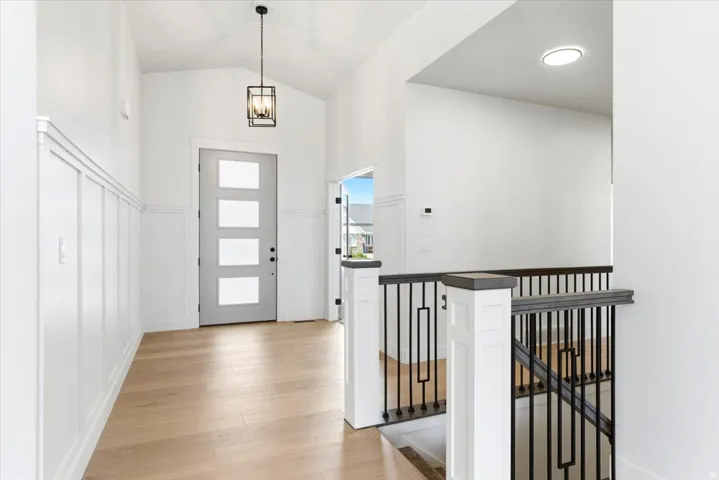 Vaulted entry featuring board and batten wainscoting, wood-finish flooring, a contemporary front door with frosted glass panels, and a modern geometric pendant light