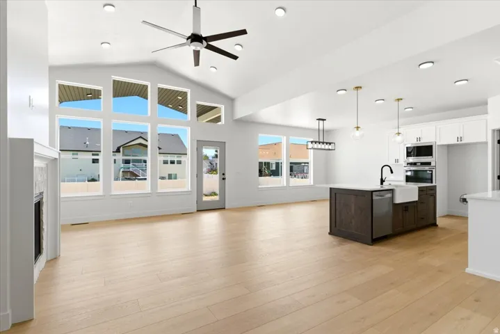 Spacious open-concept living area featuring vaulted ceilings, a modern ceiling fan, wood-finish flooring, a built-in fireplace, and a kitchen island with a farmhouse sink
