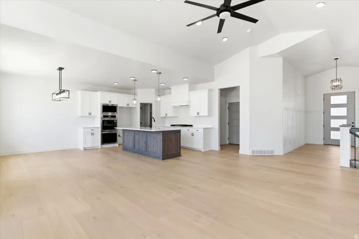 Vaulted ceilings, light wood-finish flooring, white cabinetry, a kitchen island with seating, and built-in double ovens