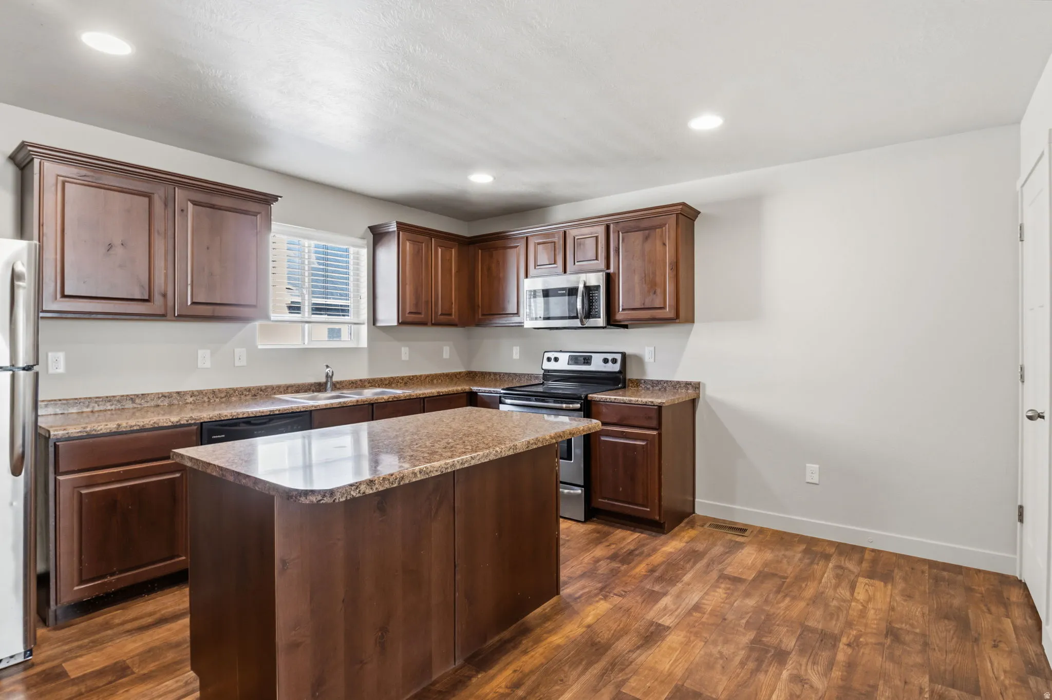 Kitchen featuring wood-finish flooring, recessed lighting, wood cabinetry, stone-finish countertops, and a central island