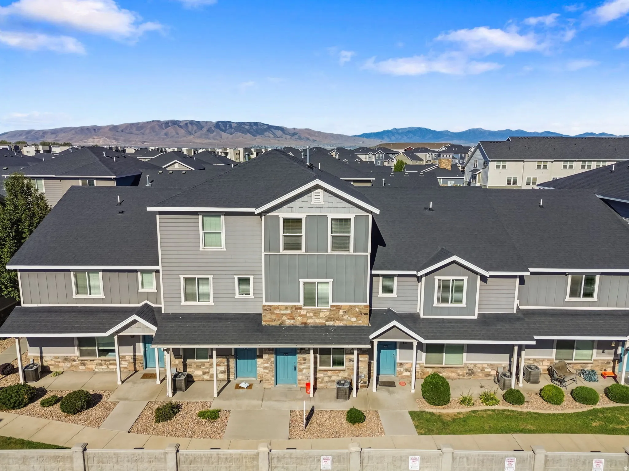Townhome exterior featuring stone accents, blue entry doors, a covered porch, and a gravel landscape