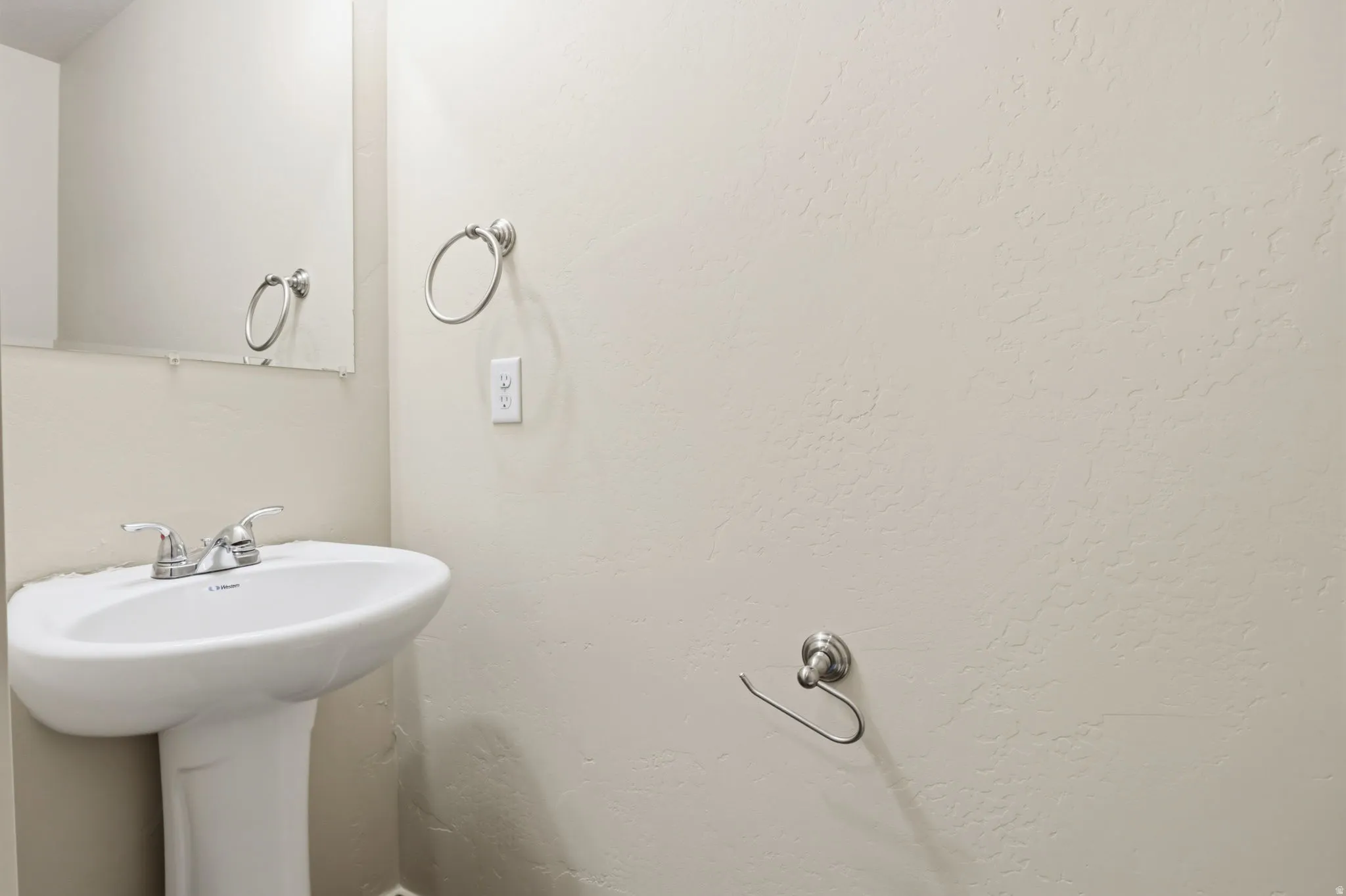Pedestal sink with chrome faucet, wall-mounted mirror, and brushed nickel hardware