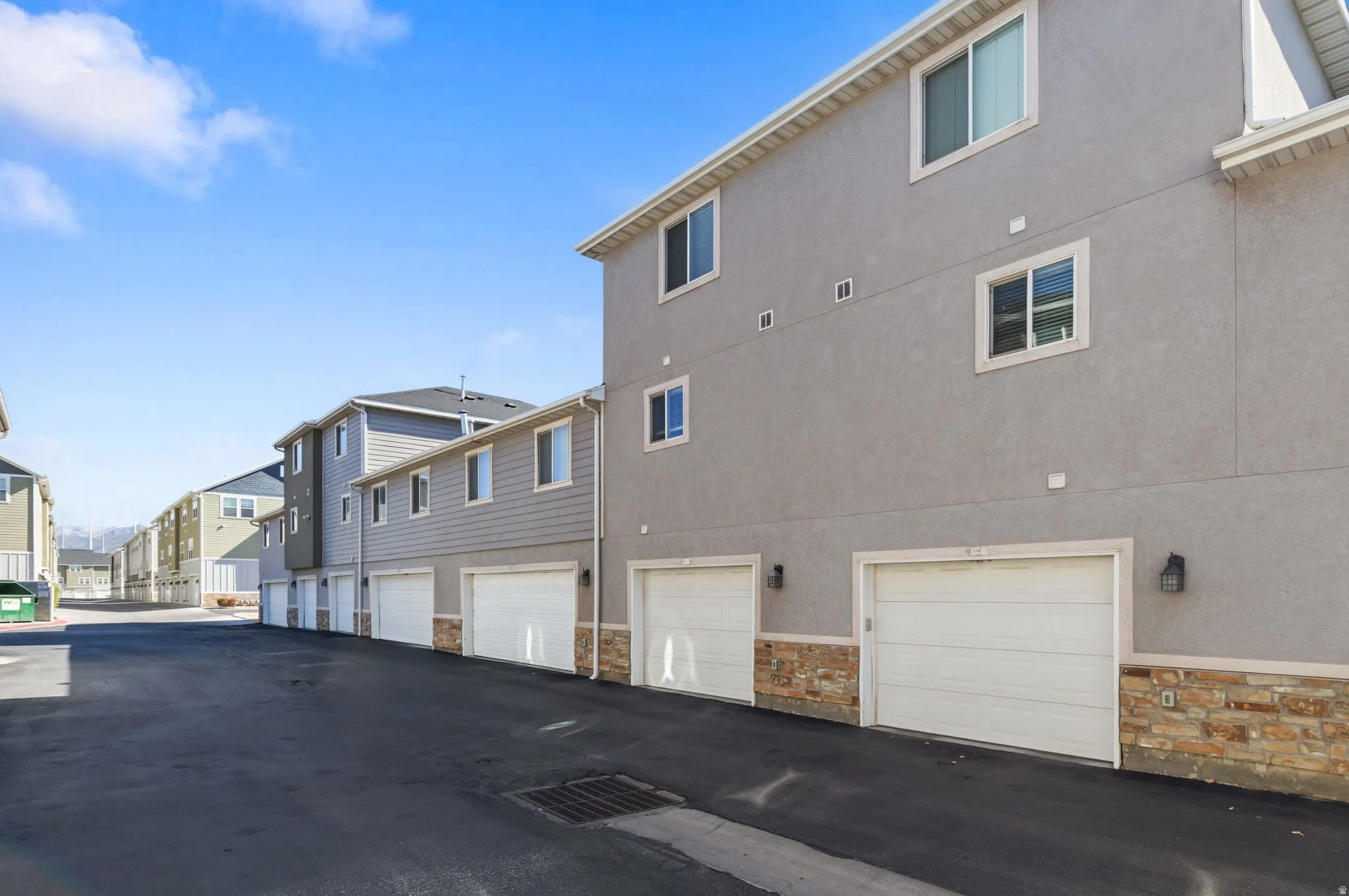 Attached garage with white door, stone veneer accent, and exterior lighting
