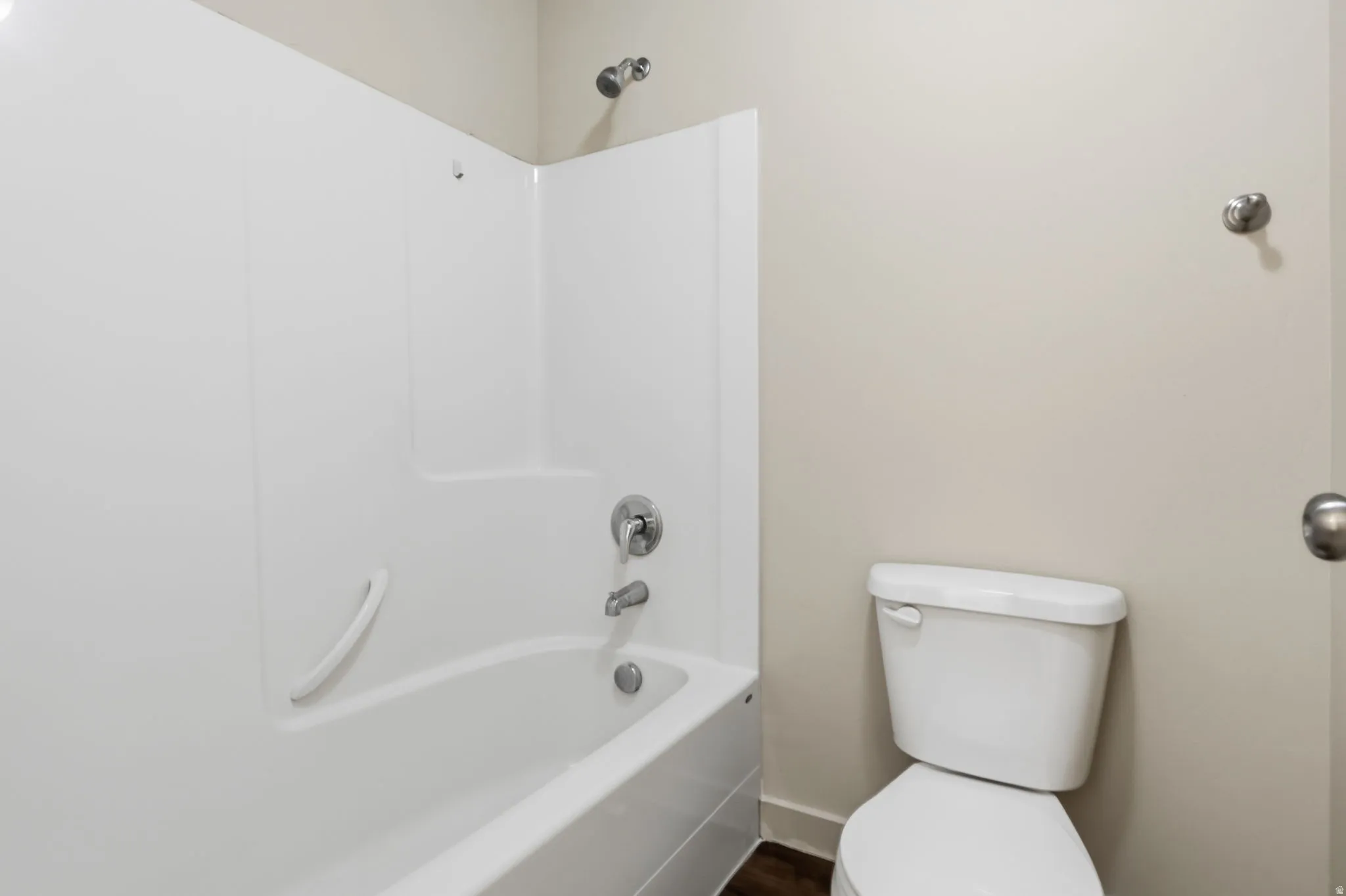 White tub with integrated shower surround, chrome plumbing fixtures, white toilet, and neutral wall paint