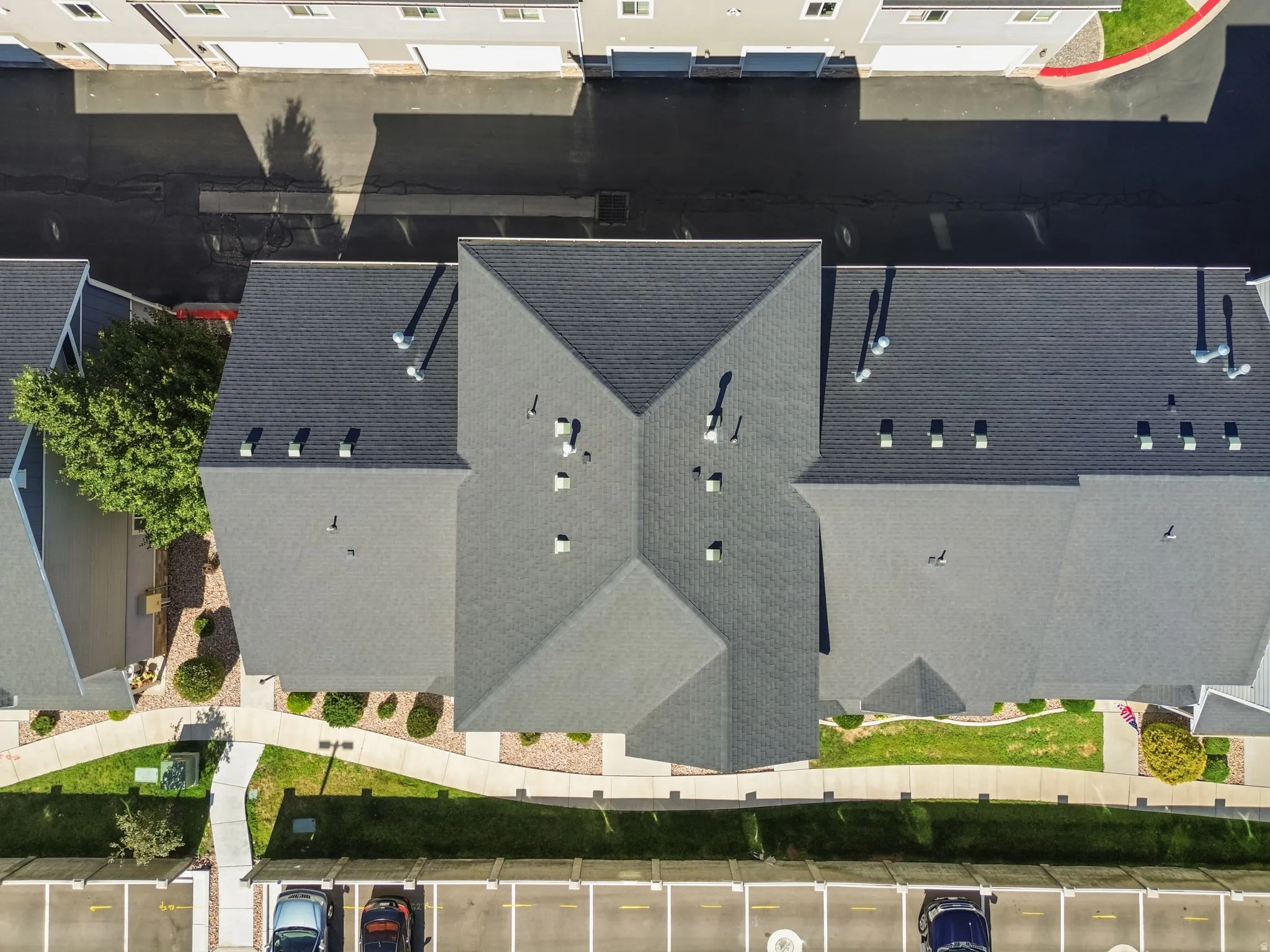 Pitched shingle roofing with multiple ventilation fixtures, surrounding landscaped grounds, and dedicated parking spaces
